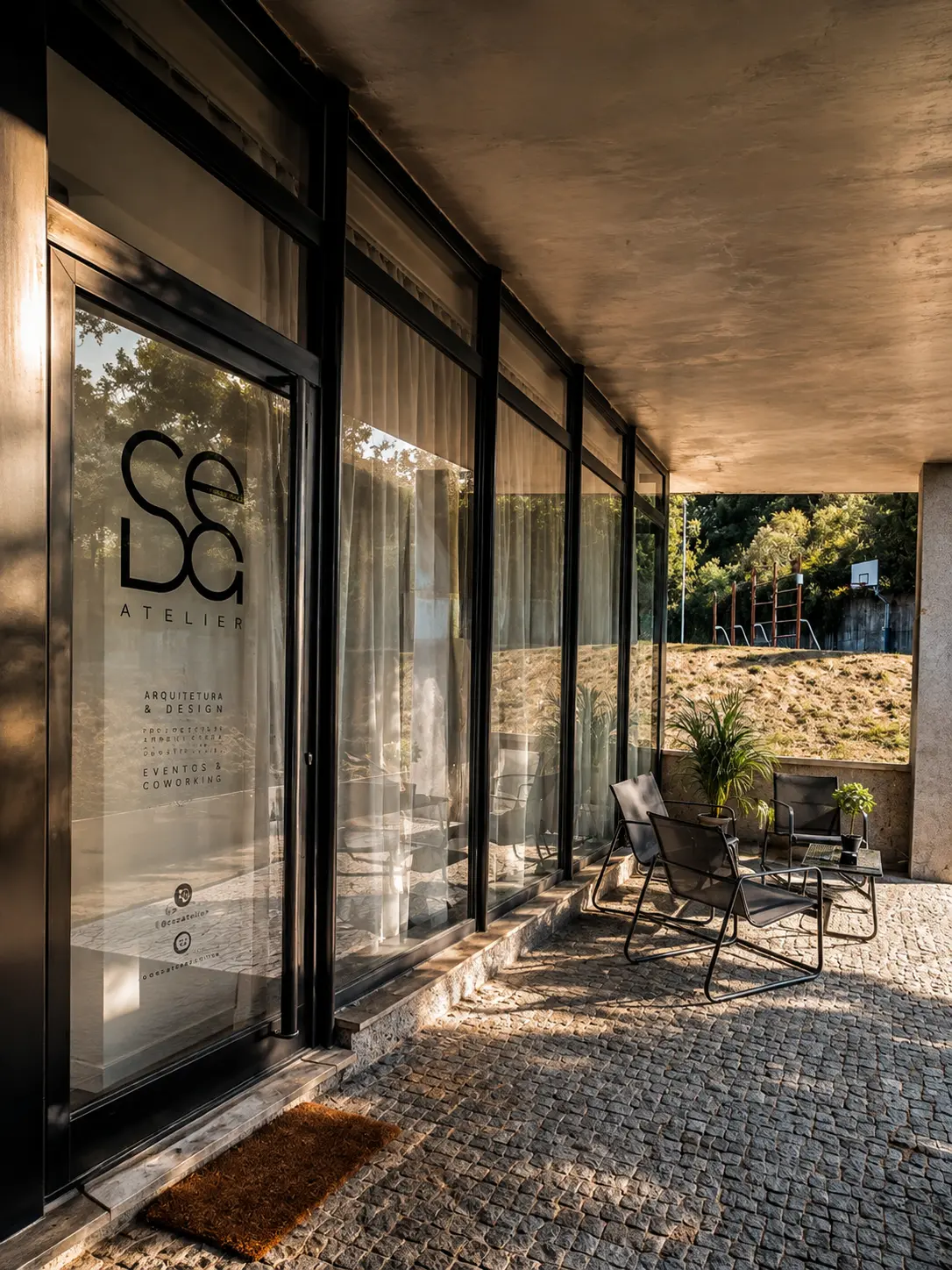 Fachada envidraçada da Seda com logótipo e esplanada com cadeiras em calçada portuguesa