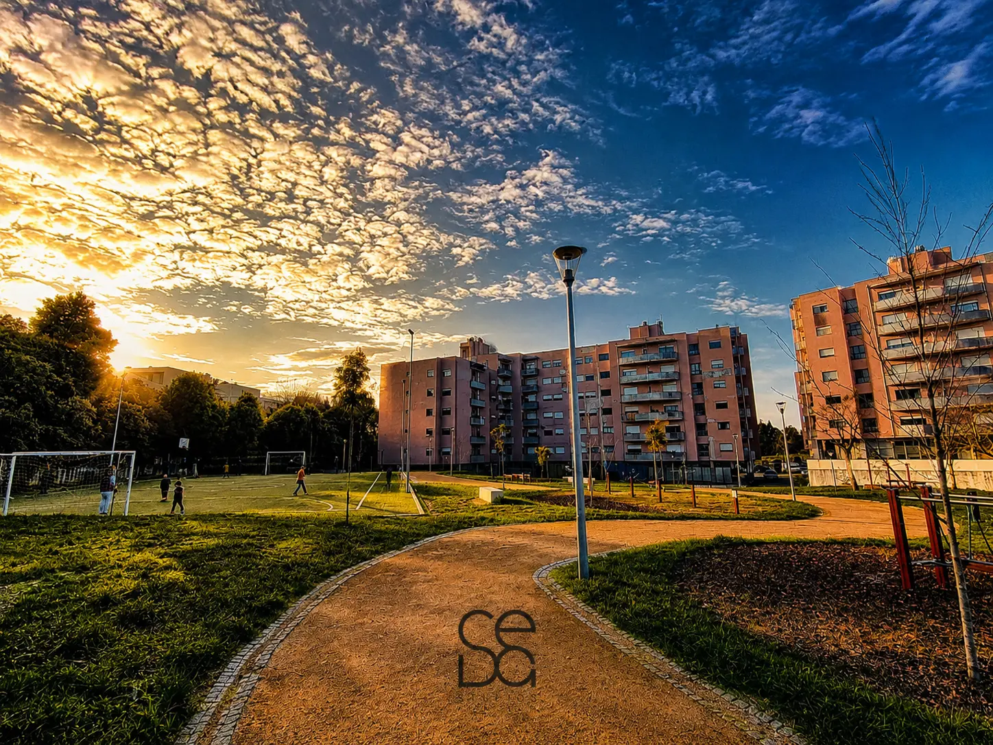 Parque urbano na envolvente do espaço, ao final do dia, com campo de jogos e edifícios